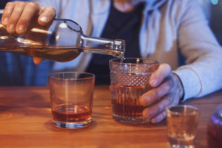 Senior man pouring drink into glass late in the evening at home, closeupの写真素材