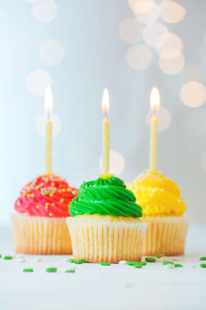 Tasty Birthday cupcakes with burning candles on table against defocused lightsの写真素材