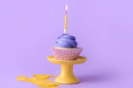 Stand with tasty Birthday cupcake and burning candle on color backgroundの写真素材