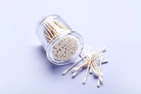 Glass with cotton swabs on color background