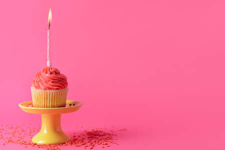 Stand with tasty Birthday cupcake and burning candle on color backgroundの写真素材
