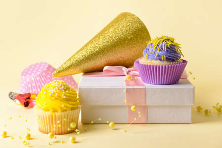 Tasty Birthday cupcakes, party hat and gift on color background