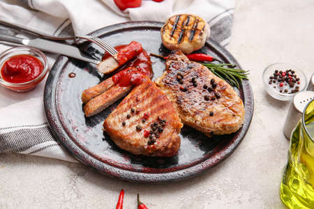 Plate with tasty steaks and spices on light background