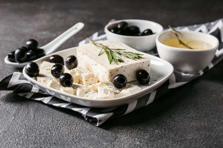Plate with tasty feta cheese, olives and rosemary on dark background