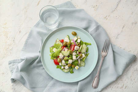 Plate with fresh Greek salad and glass of water on light backgroundの写真素材