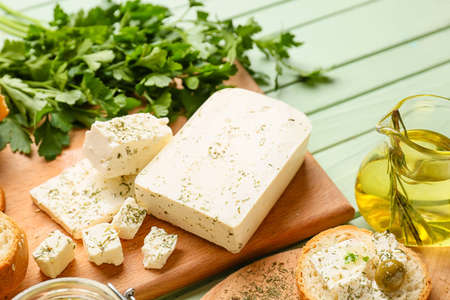 Board with tasty feta cheese, oil and parsley on color wooden background, closeupの写真素材