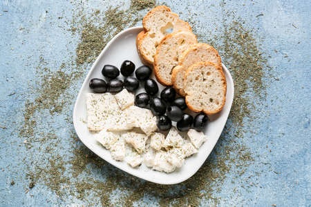 Plate with tasty feta cheese, oil, olives and bread on color backgroundの写真素材