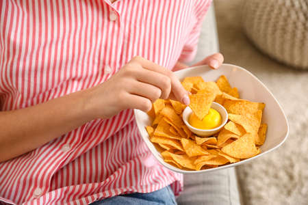Beautiful young woman eating tasty nachos at home, closeup