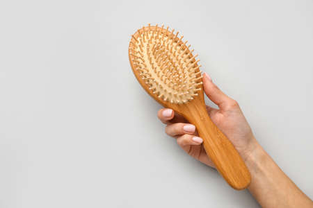 Female hand with wooden hair brush on light background