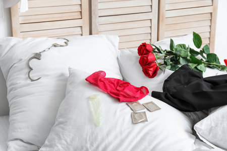 Female panties with condoms, handcuffs, roses and clothes on bed after romantic dateの写真素材