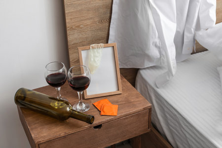 Empty bottle with glasses of wine and used condom on table in bedroomの写真素材