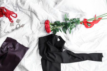 Clothes with condoms, handcuffs and flowers on bed after romantic dateの写真素材