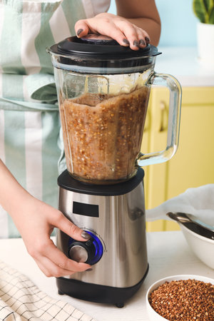 Woman preparing tasty buckwheat milk on kitchen table, closeup