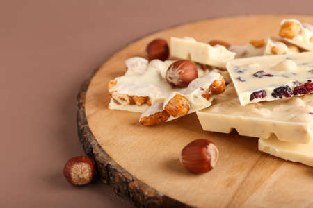 Wooden board with pieces of white chocolate and nuts on color backgroundの写真素材