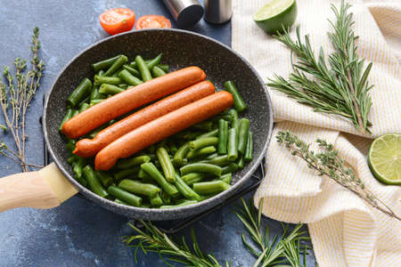 Frying pan with tasty sausages and green beans on color background, closeupの写真素材