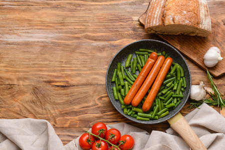 Frying pan with tasty sausages and vegetables on wooden backgroundの写真素材