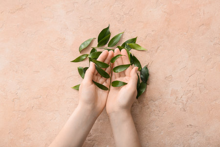 Female hands with green tea leaves on color backgroundの写真素材