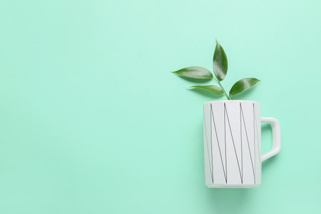 Cup and green tea leaves on color background