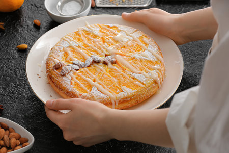 Woman holding plate with tasty orange pie on dark background