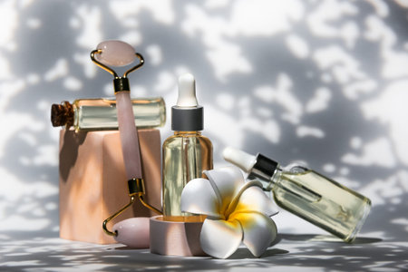 Bottles of cosmetic products with facial massage tool and flower on dark backgroundの写真素材
