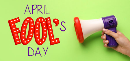 Female hand with funny megaphone on color background. April Fool's Day celebration