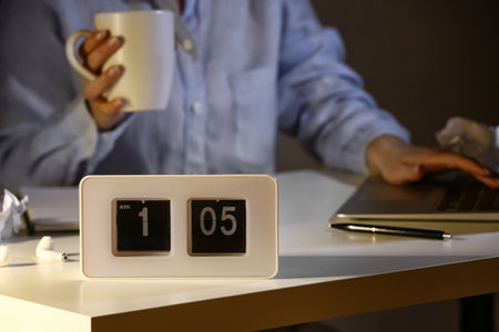 Alarm clock on table of woman working at night, closeup