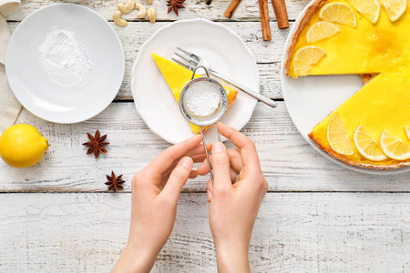 Woman decorating tasty lemon tart with sugar powder on tableの写真素材