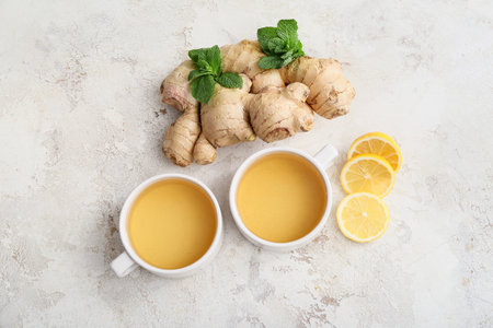 Cups of tea with ginger, mint and lemon on light background