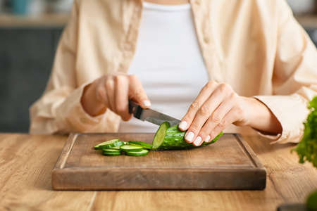 Young woman cutting cucumber in kitchenの写真素材