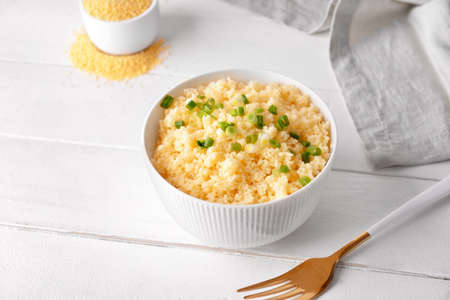Bowl with tasty couscous and green onion on light wooden backgroundの写真素材