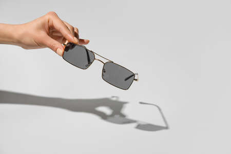Female hand with stylish sunglasses on light backgroundの写真素材