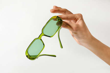 Female hand with stylish sunglasses on light backgroundの写真素材
