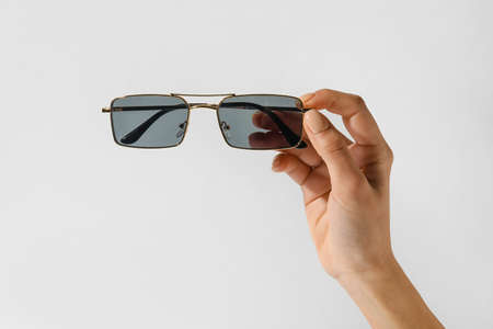 Female hand with stylish sunglasses on light backgroundの写真素材