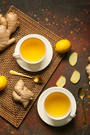 Cups of tea with ginger, spoons and lemons on grunge backgroundの写真素材