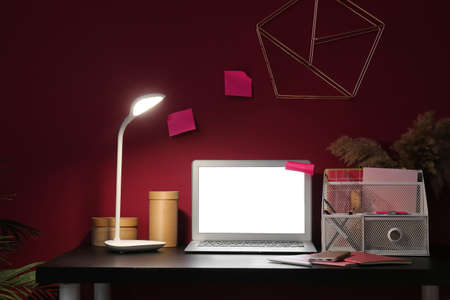Modern workplace with laptop and glowing lamp in dark room