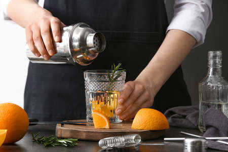 Woman making orange cocktail with rosemary on table in kitchenの写真素材