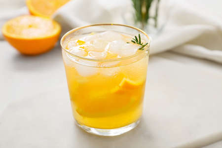 Glass of tasty orange cocktail with rosemary on light background, closeupの写真素材