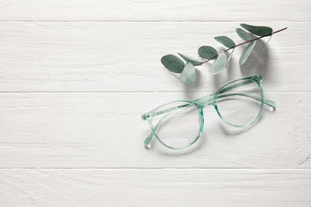 Stylish eyeglasses and eucalyptus branch on white wooden backgroundの写真素材