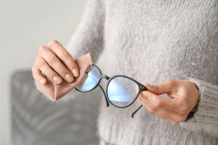 Woman wiping stylish eyeglasses at home, closeupの写真素材
