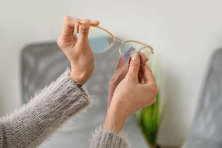 Woman wiping stylish eyeglasses at home, closeupの写真素材