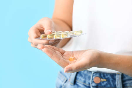 Young woman taking fish oil pills on color background, closeupの写真素材