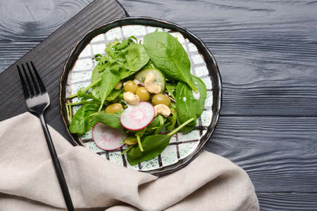 Plate with healthy salad and cashew on dark wooden background