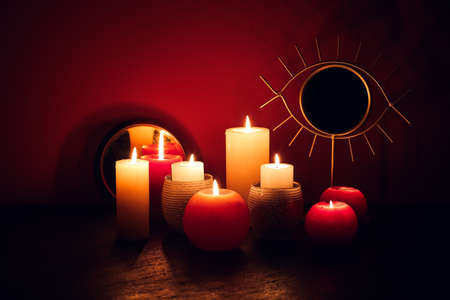 Burning candles and mirror on table near color wall
