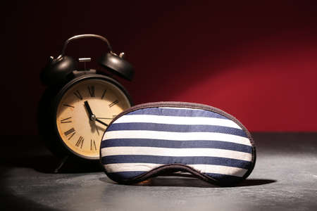 Sleeping mask with alarm clock on table near color wallの写真素材