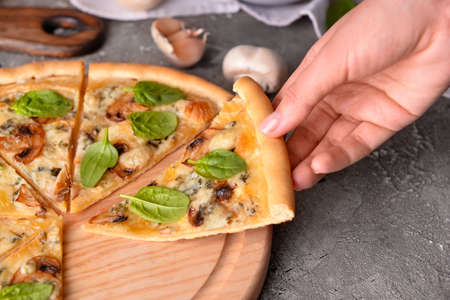 Female hand taking slice of tasty pizza on grunge background, closeup
