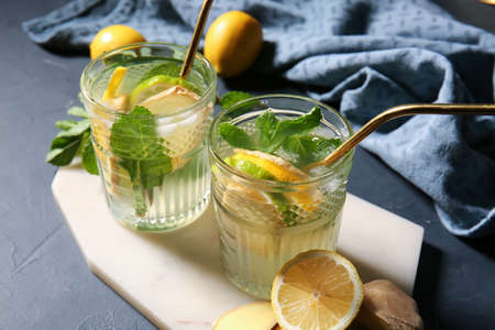 Board with glasses of ginger lemonade on dark background