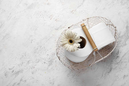 Basket with rolls of toilet paper and flower on light background