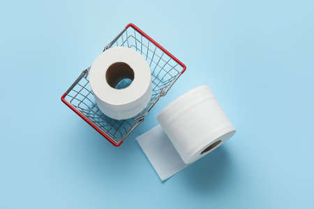 Shopping basket with rolls of toilet paper on color backgroundの写真素材
