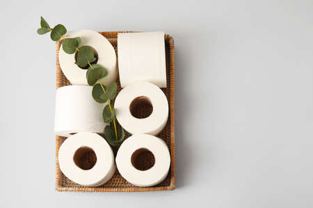 Basket with rolls of toilet paper and eucalyptus branch on gray background