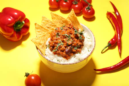 Bowl with tasty chili con carne, rice, nachos and vegetables on color background, closeupの写真素材